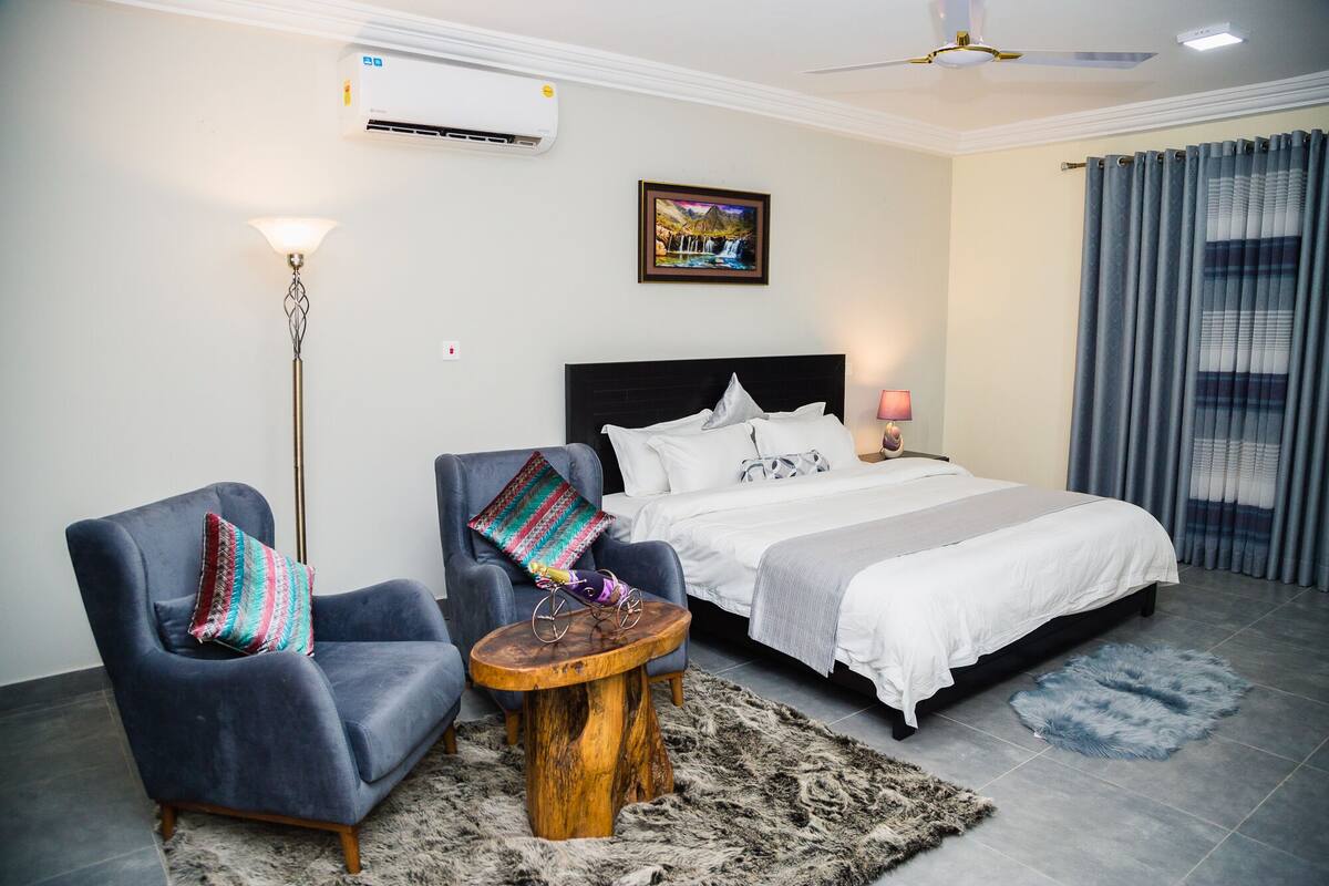 A hotel room with a bed, two armchairs, a small wooden table, a rug, and a painting on the wall.