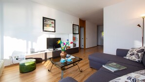 Uma sala de estar moderna com um sofá, um banquinho e uma mesa de centro de vidro com um vaso de flores.