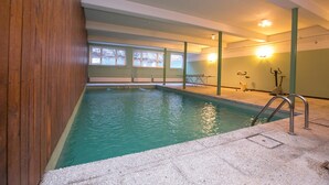 Una piscina interior con pared de madera, suelo de baldosas y ventana con vista a árboles.