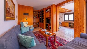 Una sala de estar con un sofá, una mesa de centro y una estantería. Hay un cuadro en la pared y una ventana al fondo.