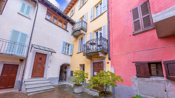 A narrow street with buildings, a wooden door, and potted plants. - Casa Gialla (Arogno)