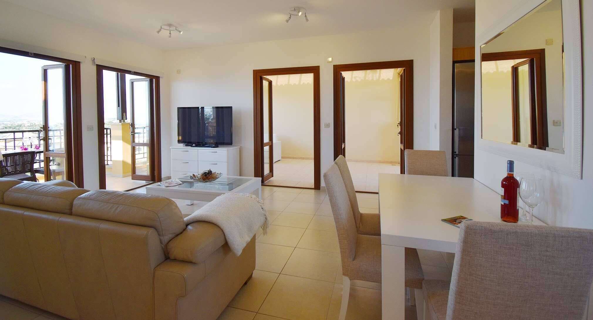 A modern living room with a sofa, a TV, a dining table, and a balcony with a view.