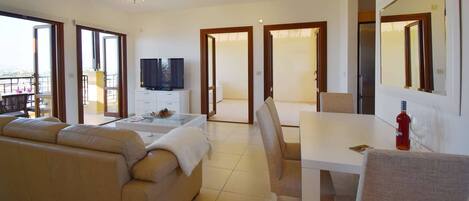 A modern living room with a sofa, a TV, a dining table, and a balcony with a view.