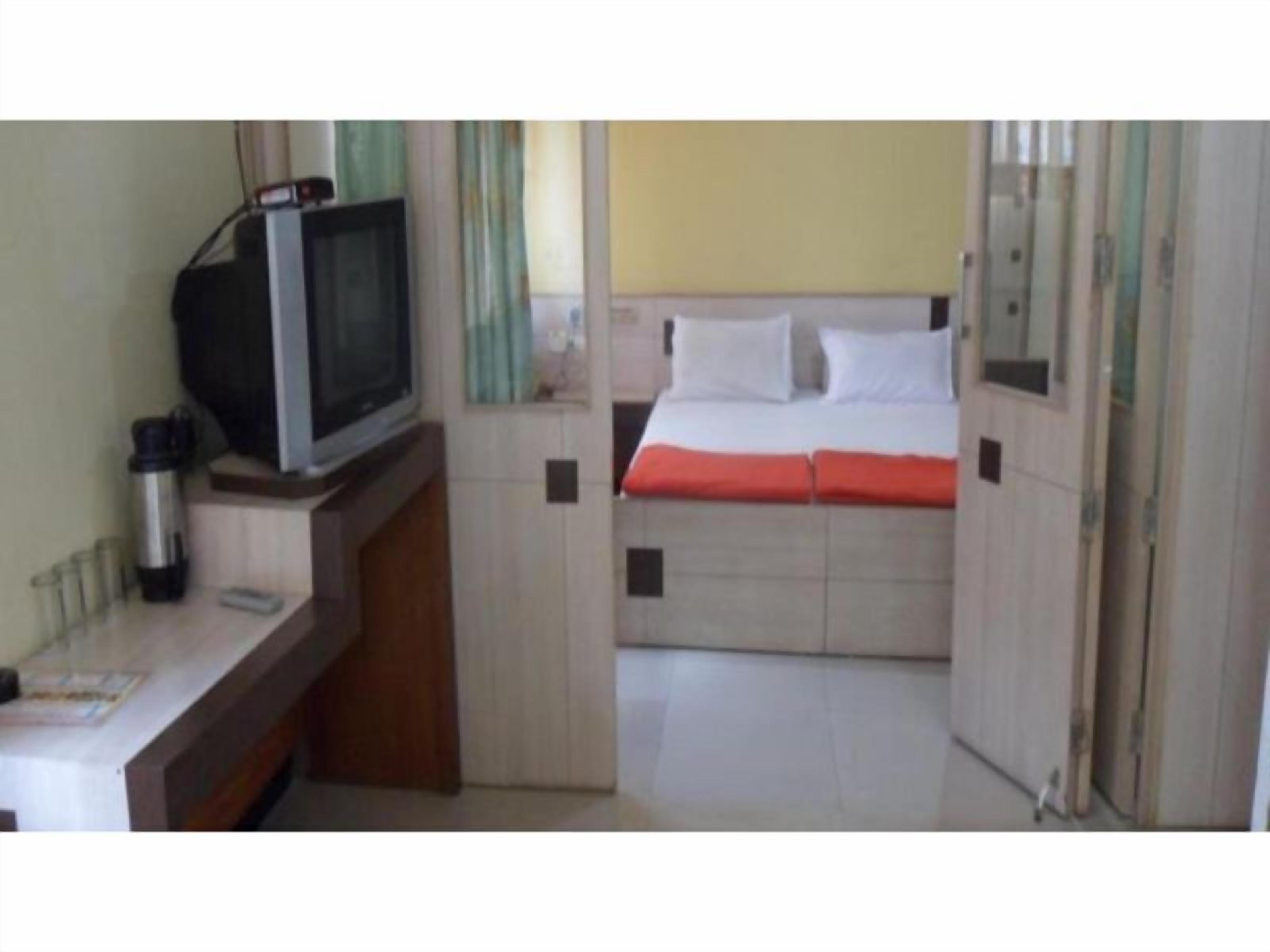Une chambre d’hôtel de taille réduite, comprenant un lit, une télévision, un petit bureau et une table de chevet.