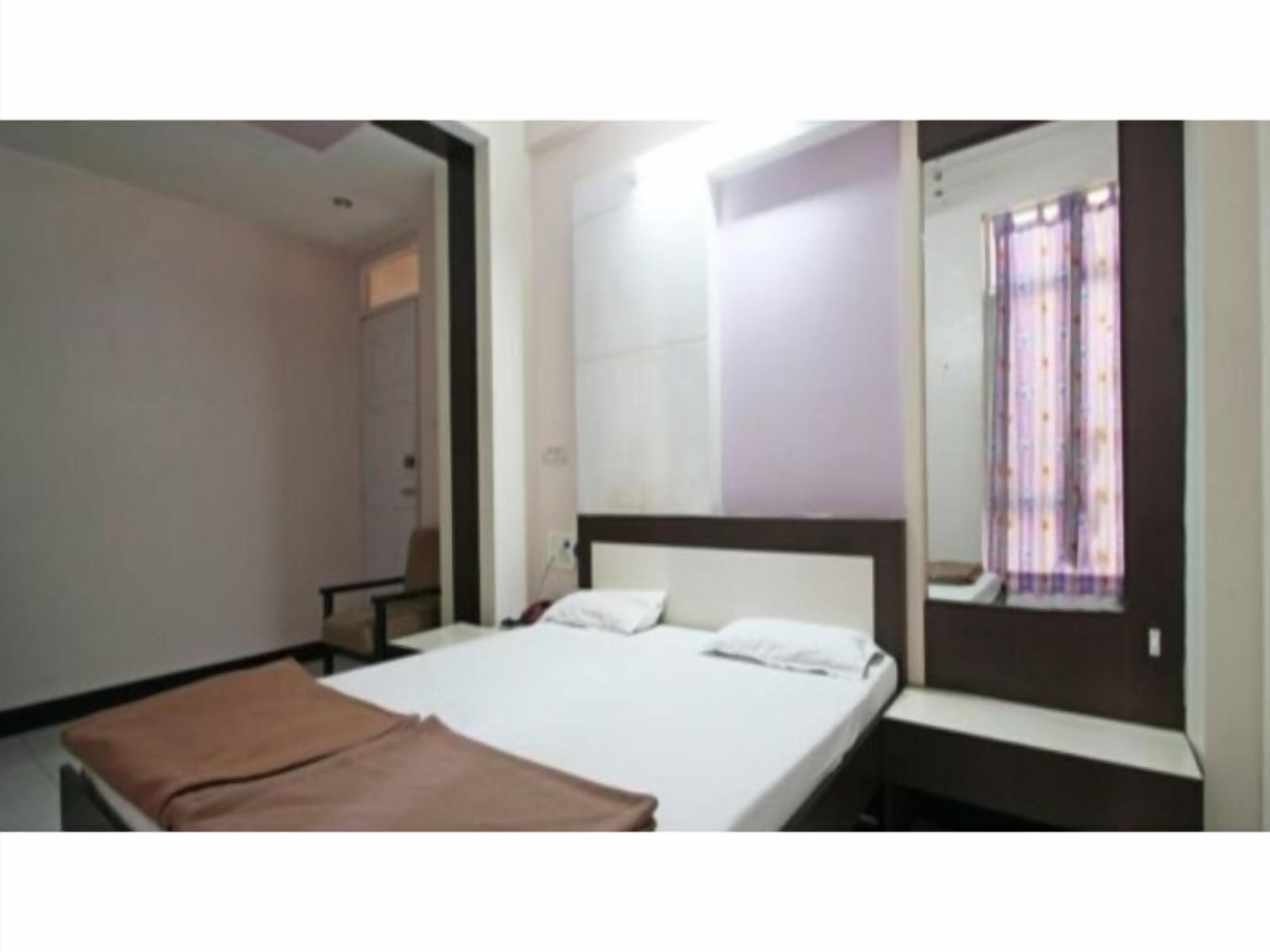 A hotel room with a single bed, a bedside table, a chair, and a large mirror.