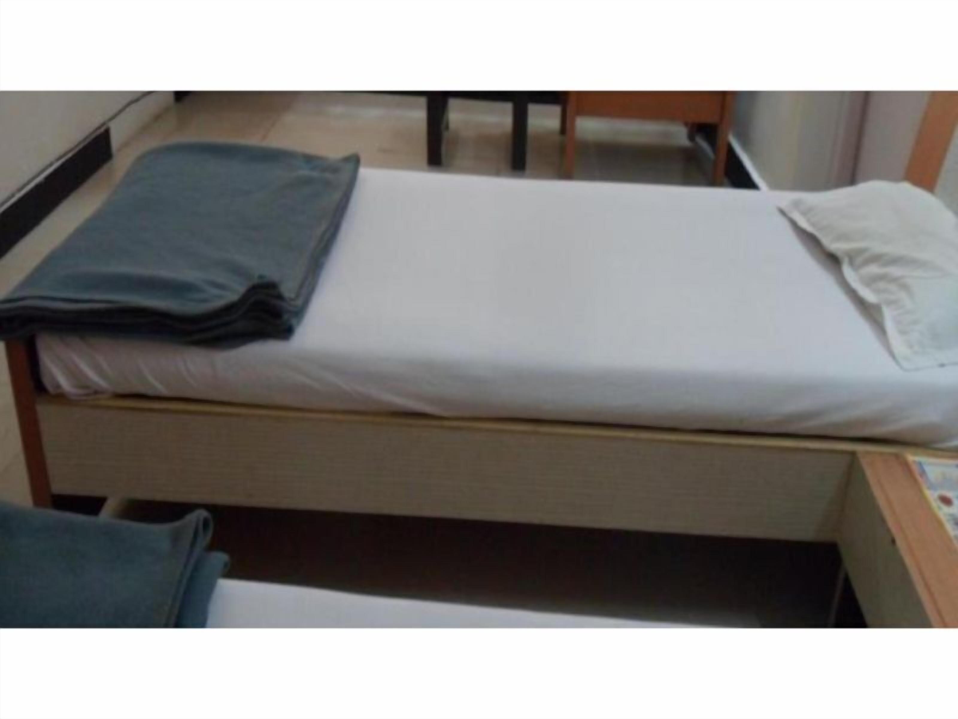 A single bed with a white mattress and a gray blanket.