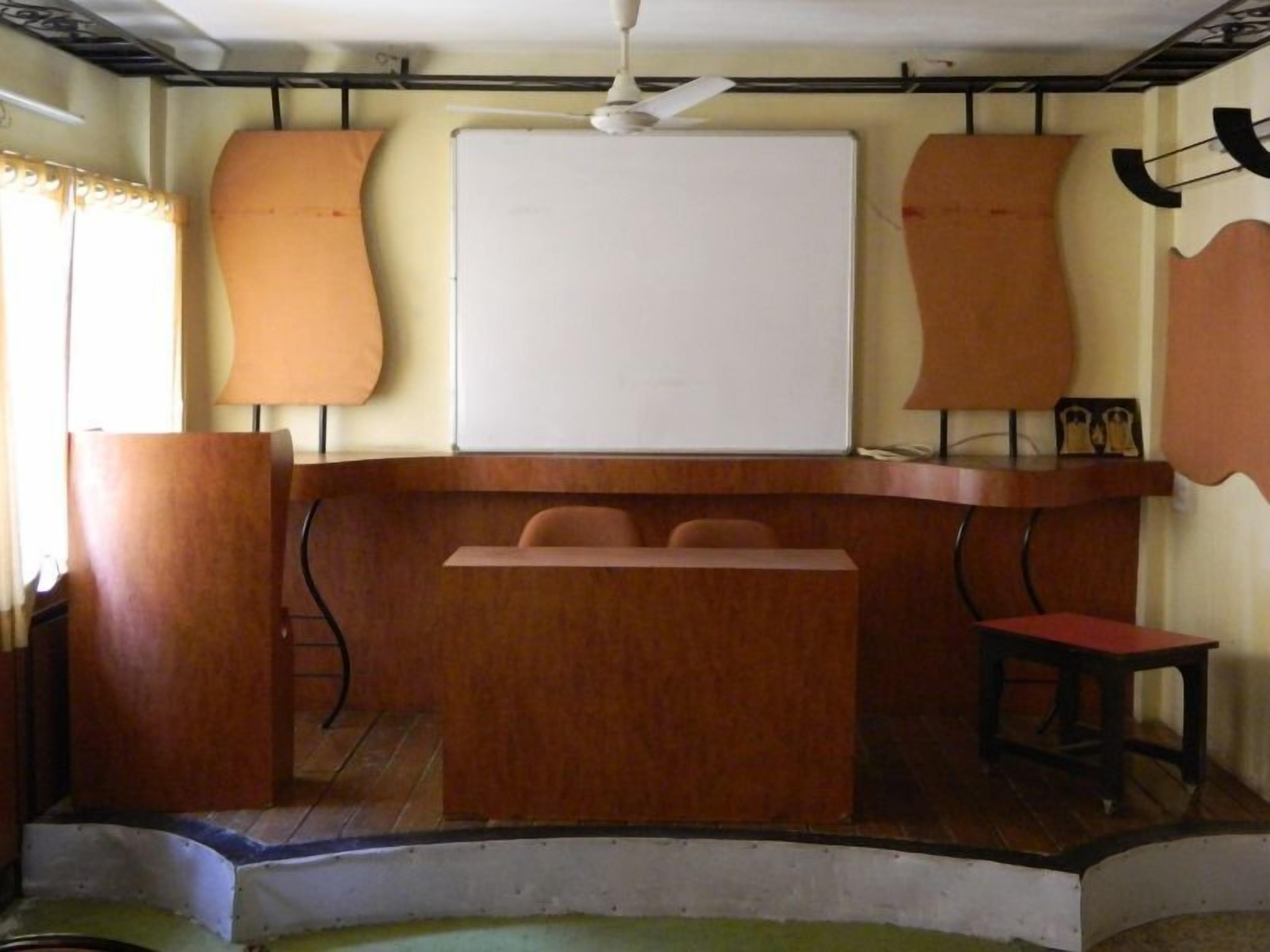 A conference room with a whiteboard, a podium, and a few chairs.