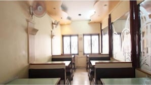 Un'aula con file di banchi e sedie, ampie finestre e una ventola a soffitto.