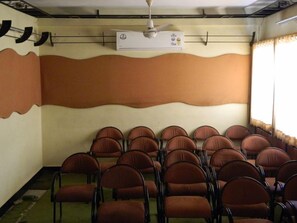 A conference room with rows of brown chairs, a ceiling fan, and an air conditioning unit on the wall. - Hotel Vaishali (Nashik)