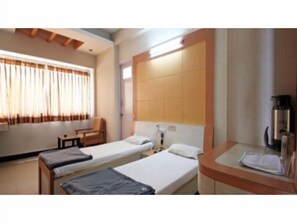 A hotel room with two single beds, a small desk, a chair, a coffee machine, and a window with curtains. - Hotel Vaishali (Nashik)