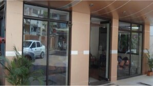 Ingresso di un edificio con porte in vetro, un'auto parcheggiata all'esterno e una pianta in vaso sul primo piano.