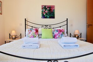 A neatly made bed with a floral pillow and a green accent pillow, two bedside lamps, and a wall-mounted picture of flowers.