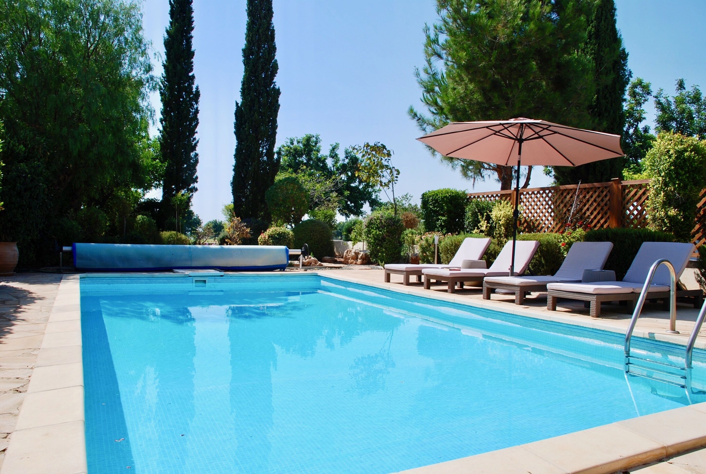 A rectangular swimming pool with a clear blue surface, surrounded by lounge chairs and an umbrella.