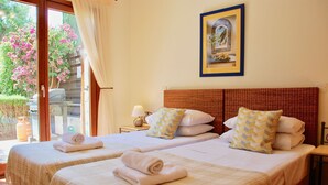A hotel room with two beds, a view of the garden, a painting on the wall, and a table with a lamp. - Villa HG28 - Loukia (Kouklia)