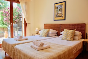 Habitación de hotel con dos camas, vista al jardín, un cuadro en la pared y una mesa con lámpara.