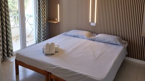 Habitación de hotel con cama, una mesita, un ventanal con cortinas y una pared con líneas verticales.