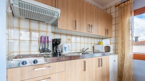 Una cocina con armarios de madera, encimera de acero inoxidable, cafetera, hervidor, microondas y un refrigerador pequeño.