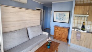 Una sala de estar con sofá, una mesa de centro y una cocina con alacenas y estufa.