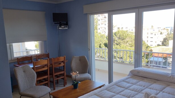 Habitación de hotel con cama, escritorio, silla, televisor y balcón con vista a edificios.