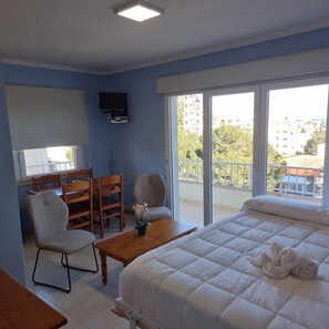 A hotel room with a bed, a desk, a chair, a TV, and a balcony with a view of buildings. - Central Apartment "Portosun Estrella" Close to the Beach (Portocolom)