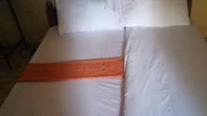 A bed with white bedding and an orange bedspread. - Jackmart Lodge - Adults Only (Nakuru)