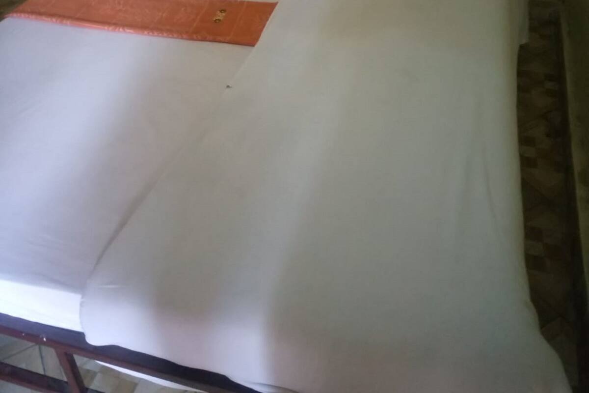 Una cama con ropa de cama blanca y una manta naranja, un cabecero de madera y una mesita a la izquierda.