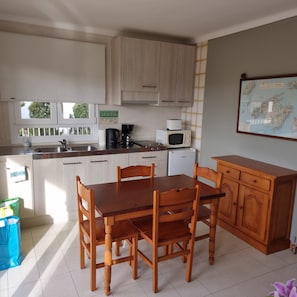 Une cuisine avec des meubles en bois, une table à manger avec des chaises, une machine à café, un four à micro-ondes et une carte accrochée au mur.