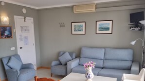 A living room with a grey sofa, a white table, and a wooden dining table. There are two chairs, a vase with flowers, and a mounted air conditioner. - Central Apartment "Portosun Caracol" Close to the Beach (portocolom)