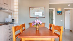 A dining area with a wooden table, chairs, a vase with flowers, a kitchen with appliances, and a framed map on the wall. - Central Apartment "Portosun Caracol" Close to the Beach (portocolom)