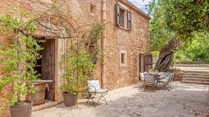 A rustic stone building with a wooden door, potted plants, outdoor seating, and a tree. - Mediterranean country house with Wi-Fi, Pool and Garden (Cala Mondrago)