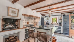 A kitchen with a fireplace, wooden beams, a large island with bar stools, and a view of the outdoors. - Mediterranean country house with Wi-Fi, Pool and Garden (Cala Mondrago)