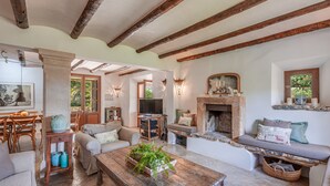 A rustic living room with exposed wooden beams, a fireplace, a television, and a dining area with wooden furniture. - Mediterranean country house with Wi-Fi, Pool and Garden (Cala Mondrago)