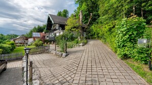 Un sentier pavé de pierres menant à un bâtiment doté d’un toit en pente, entouré de verdure et d’une clôture blanche en bois.