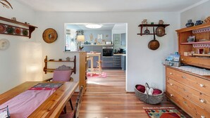 Une pièce chaleureuse avec un banc en bois, une table à manger, un panier rempli de coussins et une commode en bois dotée d’étagères.