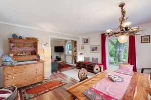 Ein gemütliches Wohnzimmer mit einem Holzesstisch, einer Chandelüster und Blick durch ein Fenster.