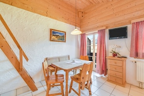 Un intérieur en bois comprenant une table à manger, des chaises, un banc, un téléviseur, un radiateur et une fenêtre avec des rideaux.