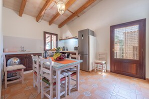 A kitchen with wooden beams, a dining table with chairs, a refrigerator, and a door with a decorative screen.