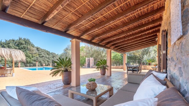 Un área de estar al aire libre techada con piscina al fondo.