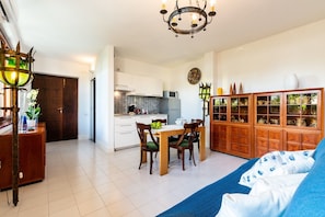 A modern kitchen with white cabinets, a dining table with chairs, a chandelier, and a cabinet with glass doors.