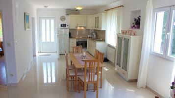 Una cocina amplia con alacenas blancas, una mesa de comedor con sillas y un ventanal con cortinas.