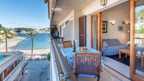 A balcony with a table, chairs, and a sofa, overlooking a beach and sea.