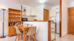 A compact kitchen with a dining table, chairs, a bookshelf, and a microwave.