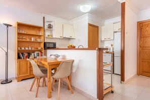 A compact kitchen with a dining table, chairs, a bookshelf, and a microwave.