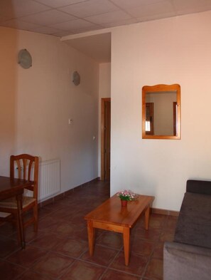 A living room with a wooden table, a sofa, a mirror, and a door leading to another room.