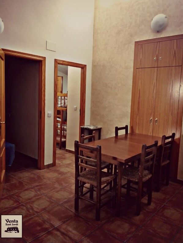 A dining area with a wooden table and chairs, a wooden cabinet, and a tiled floor.