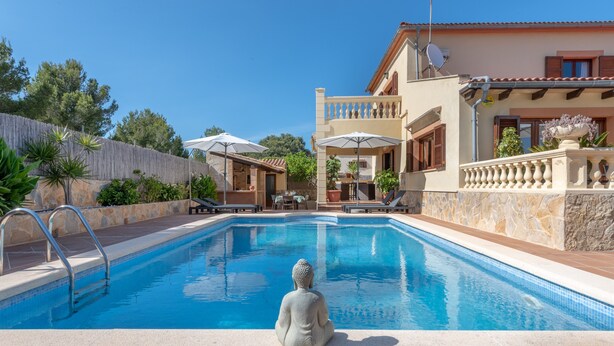 Une piscine ornée d’une statue de Bouddha, un espace extérieur aménagé pour s’asseoir et un bâtiment à deux étages doté de balcons.