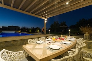 An outdoor dining area with a pool in the background, surrounded by wicker chairs and a table set for a meal.
