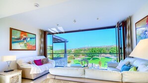 A modern bedroom with a large window, a sofa, a bedside table, and a painting on the wall. - Villa 141 - Rio (Kouklia)