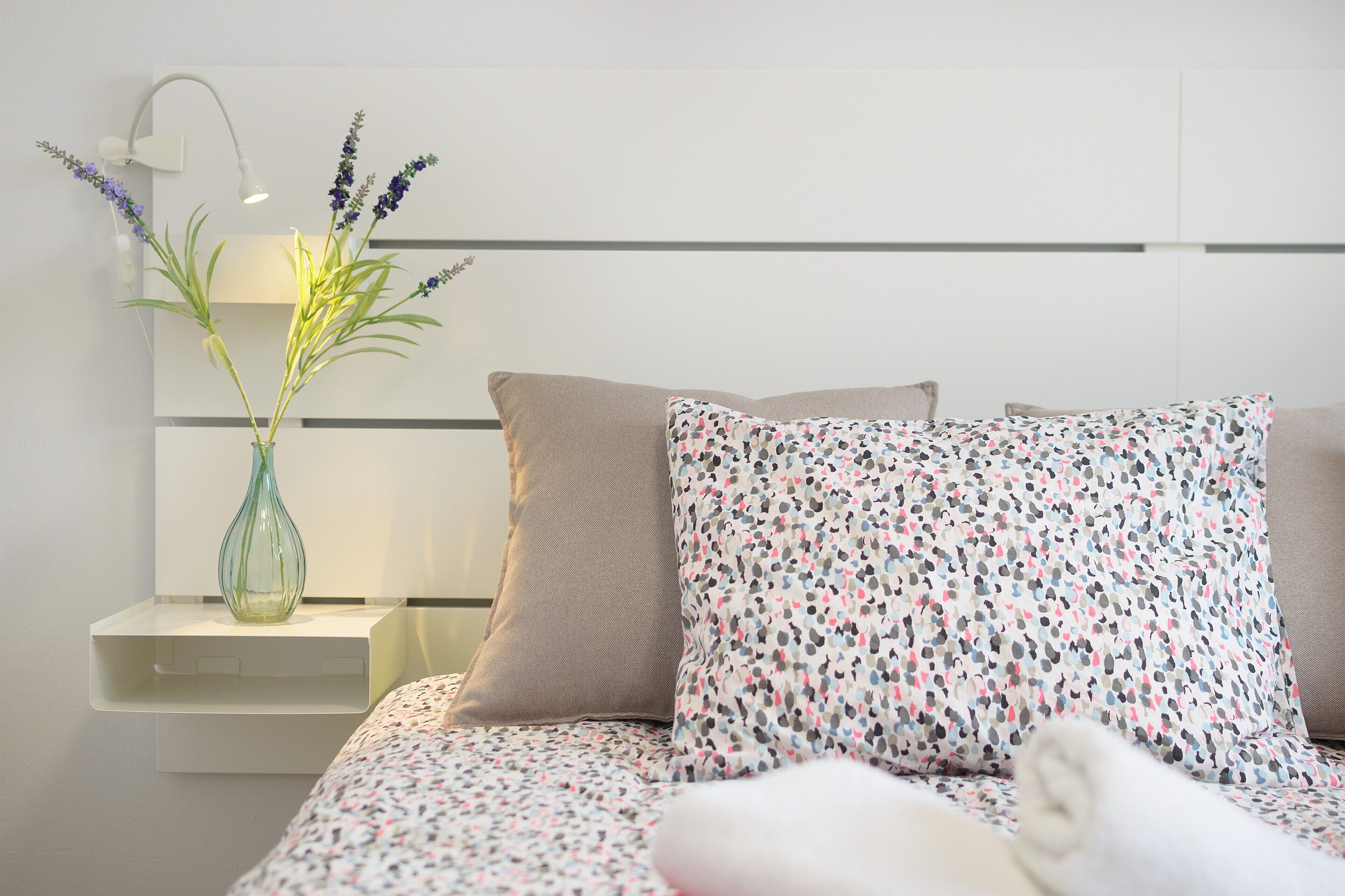 A neatly made bed with patterned bedding, a bedside lamp, and a vase with flowers on a bedside table.