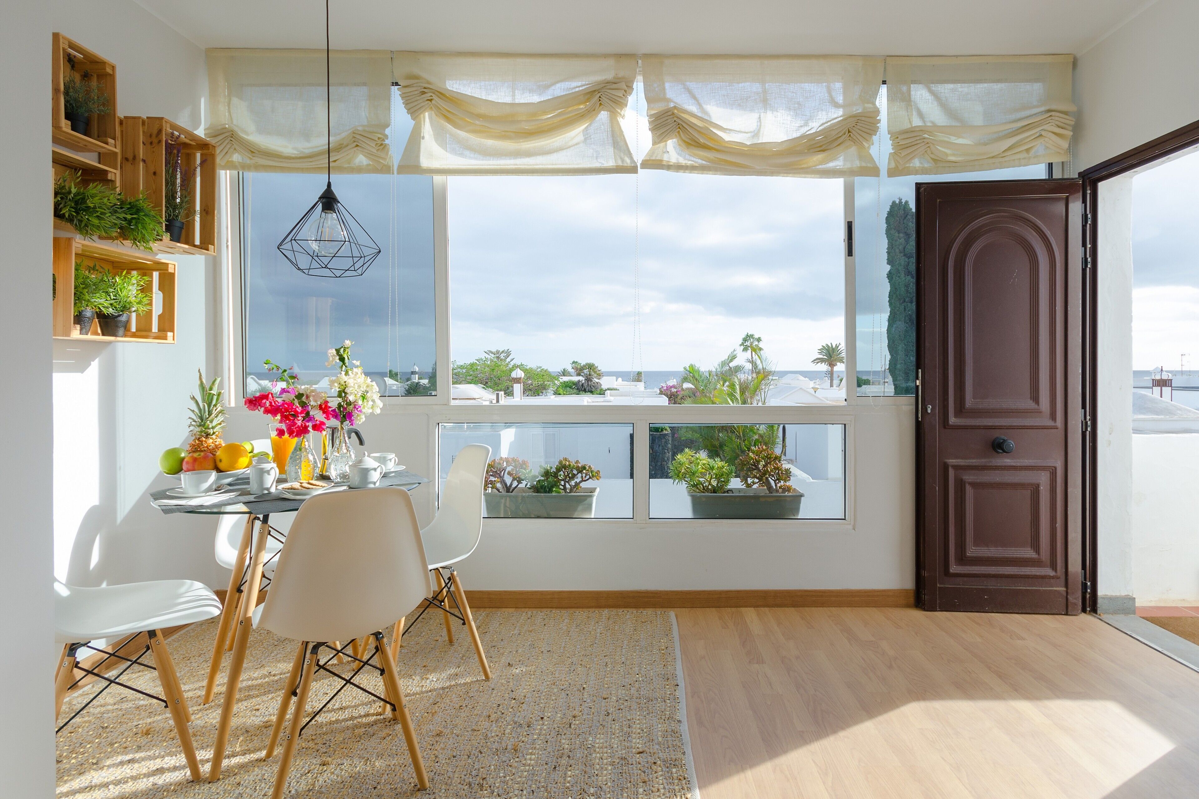 A dining area with a table, chairs, potted plants, and a view through large windows.